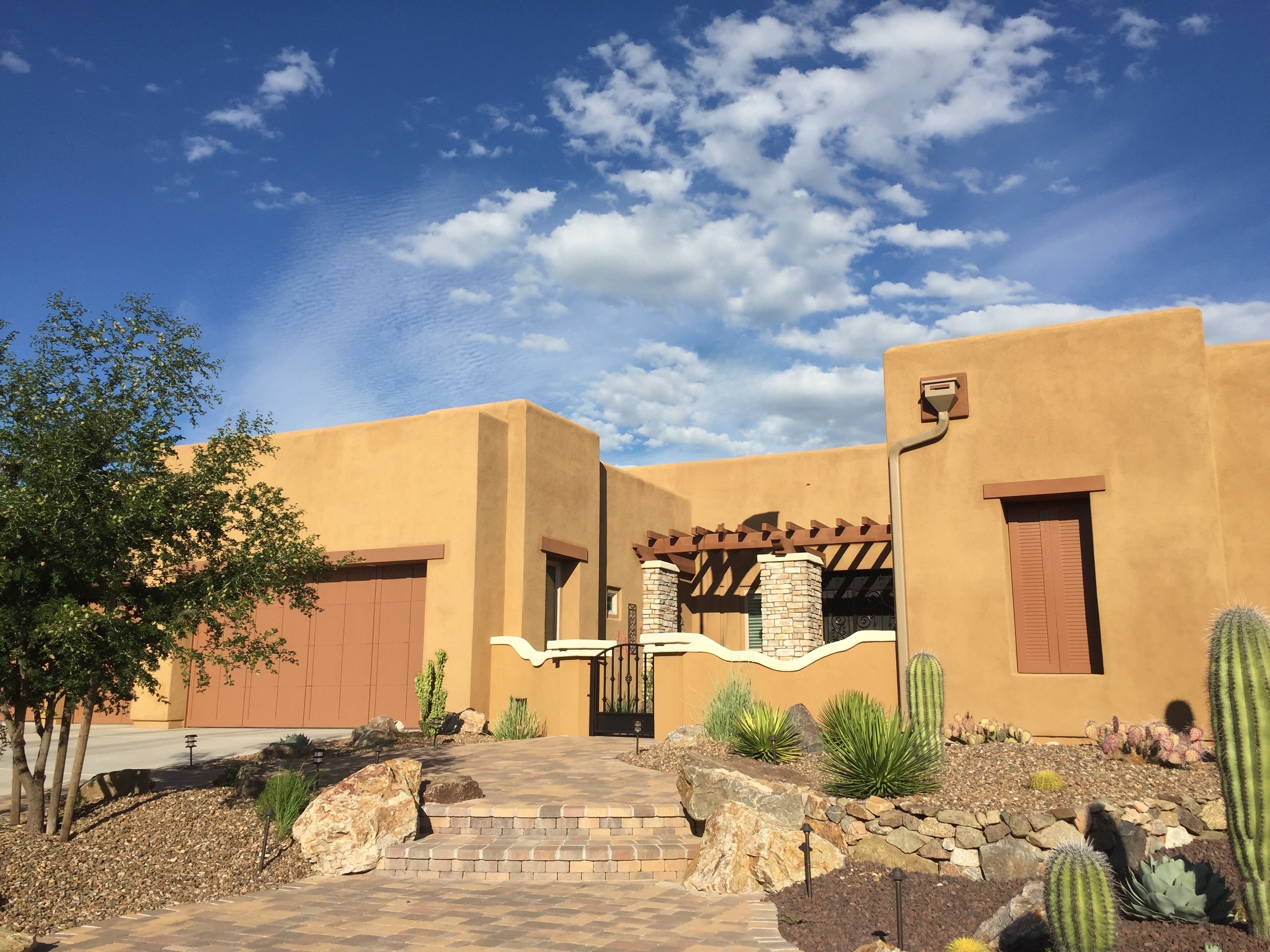 Pueblo-style stucco home with a pergola entry, saguaro, agave and a gravel desert yard under a bright blue sky